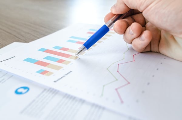 Hand holding pen reviewing business graphs