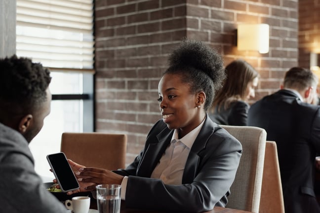 Businesswoman showing a coworker her phone at a coffeeshop